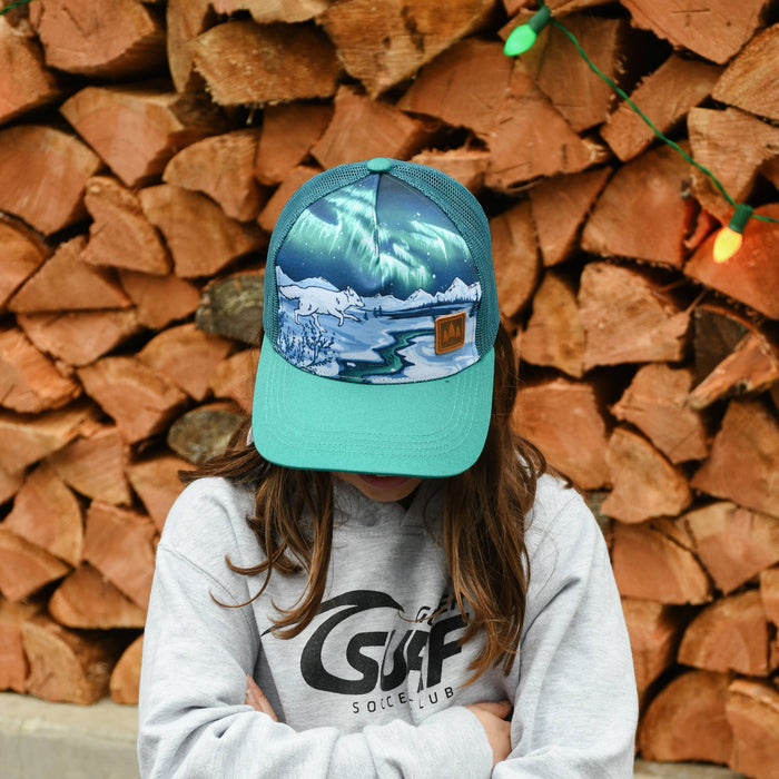 Person wearing a cap and sweatshirt with a brand logo, standing in front of stacked firewood.