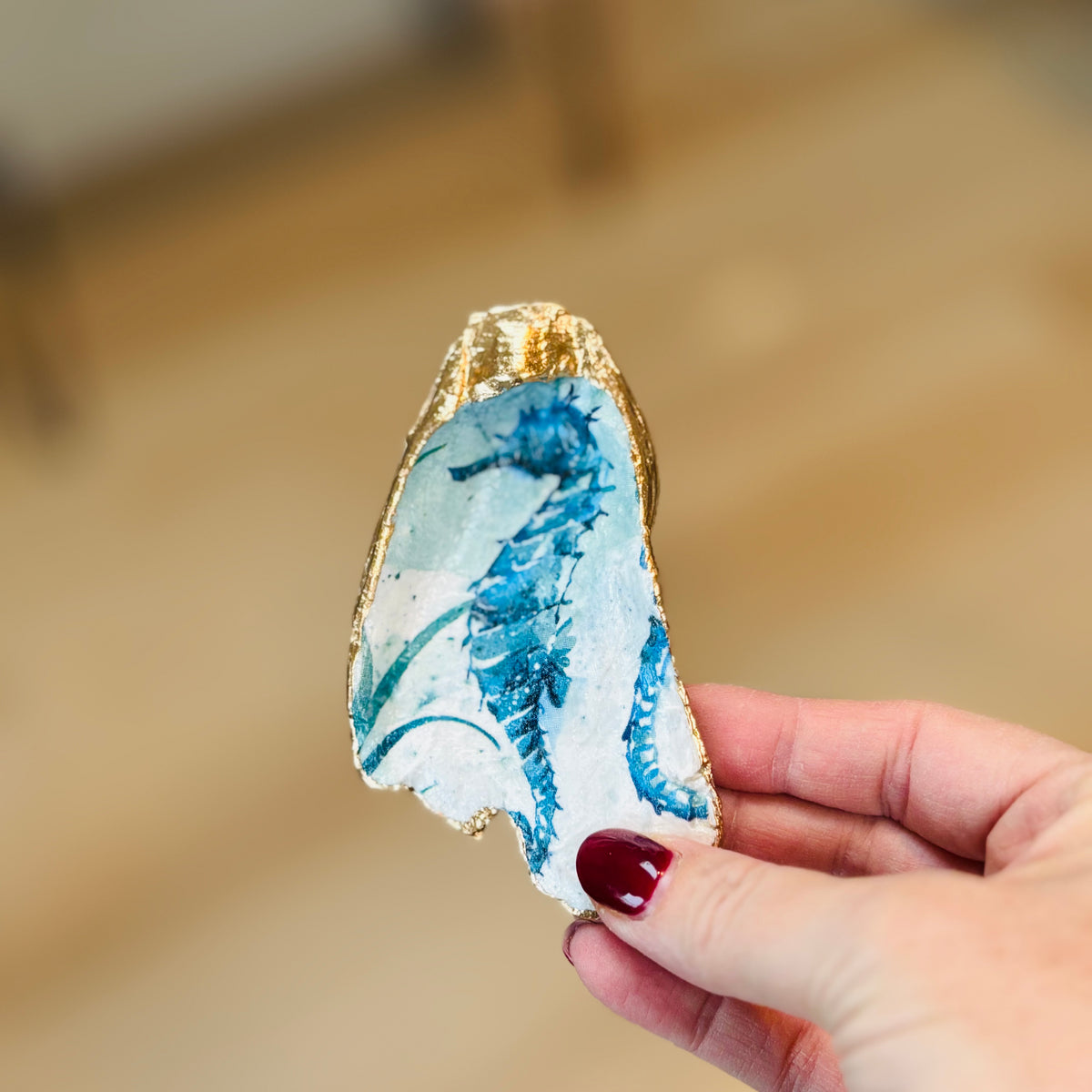 Hand holding a decorative stone with blue patterns and gold edge against a blurred background