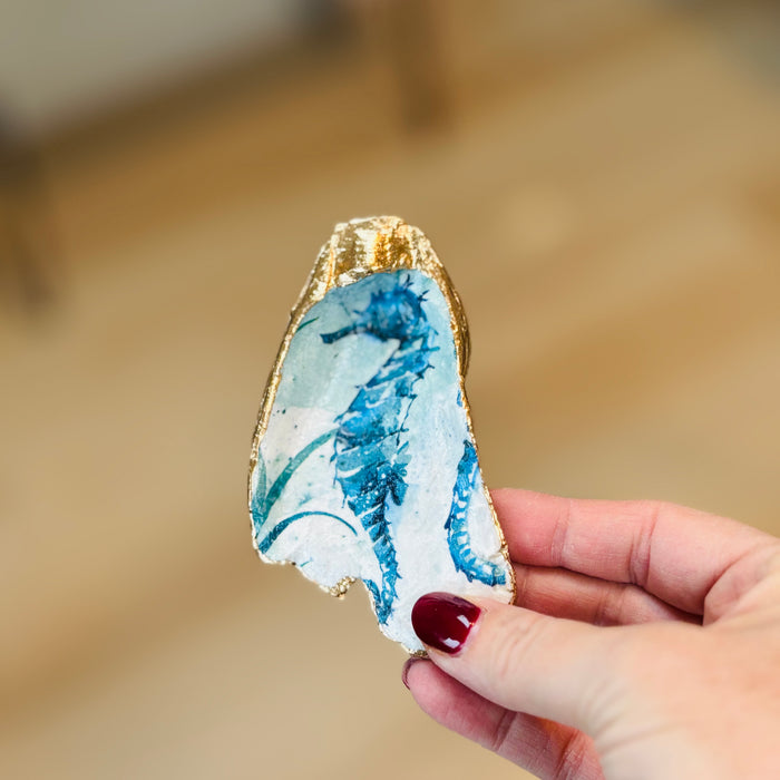 Hand holding a decorative stone with blue patterns and gold edge against a blurred background