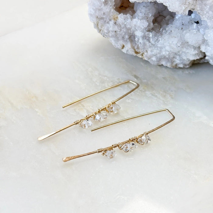 Atlantic Threader Earrings with Herkimer Diamonds in 14k gold fill with three Herkimer diamonds wire wrapped along each threader bar, flat lay on a light stone surface