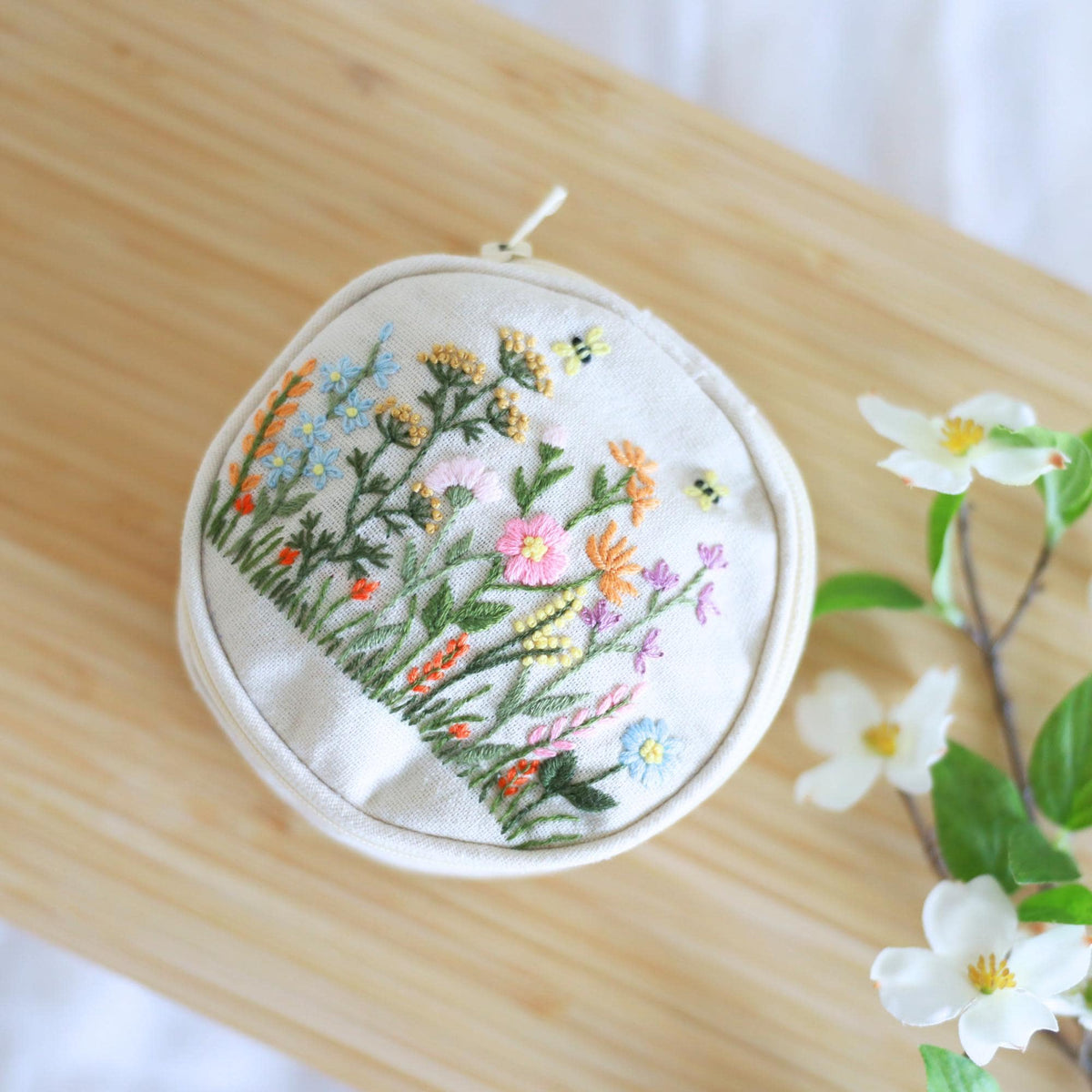 Hand embroidered jewelry pouch with wildflower embroidery, angled view on a wood table