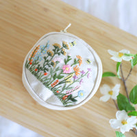 Hand embroidered jewelry pouch with wildflower embroidery, angled view on a wood table