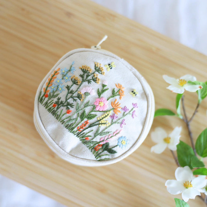 Hand embroidered jewelry pouch with wildflower embroidery, angled view on a wood table