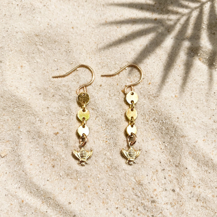 Bee Charm Coin Earrings in 14k gold fill, styled on pale sand at the beach