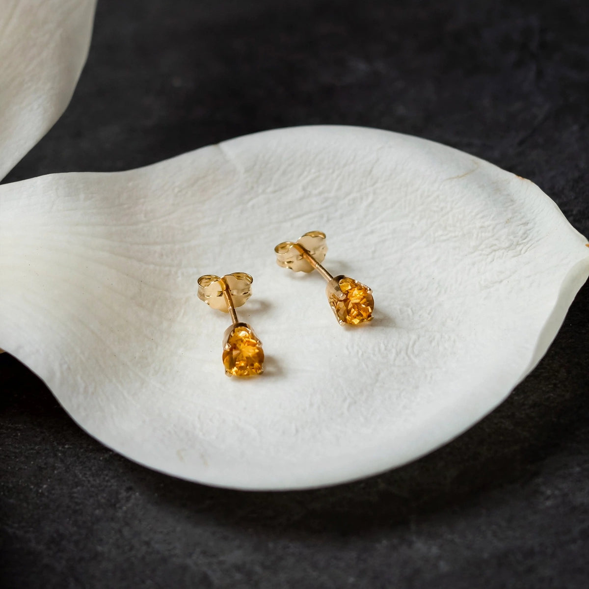 Citrine stud earrings in solid 14k gold resting on a white magnolia petal
