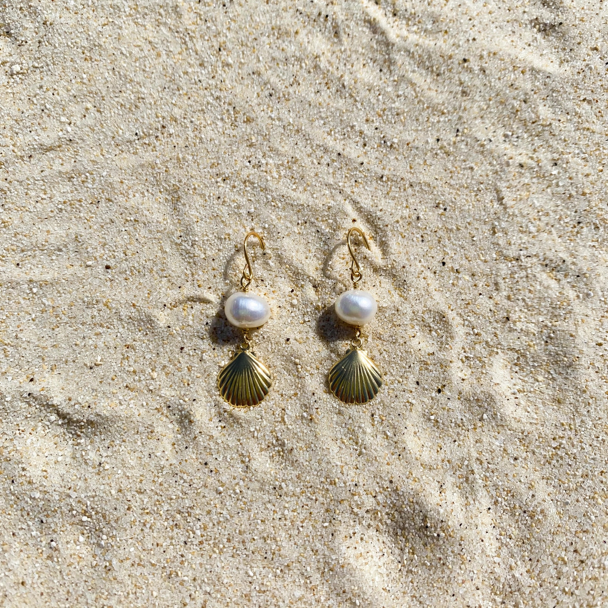 Clam Shell Pearl Earrings in 14k gold fill, styled on pale sand at the beach