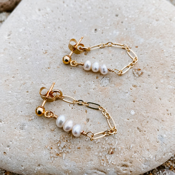Coconut Post Pearl Huggie Earrings in 14k gold fill, styled on pale sand at the beach