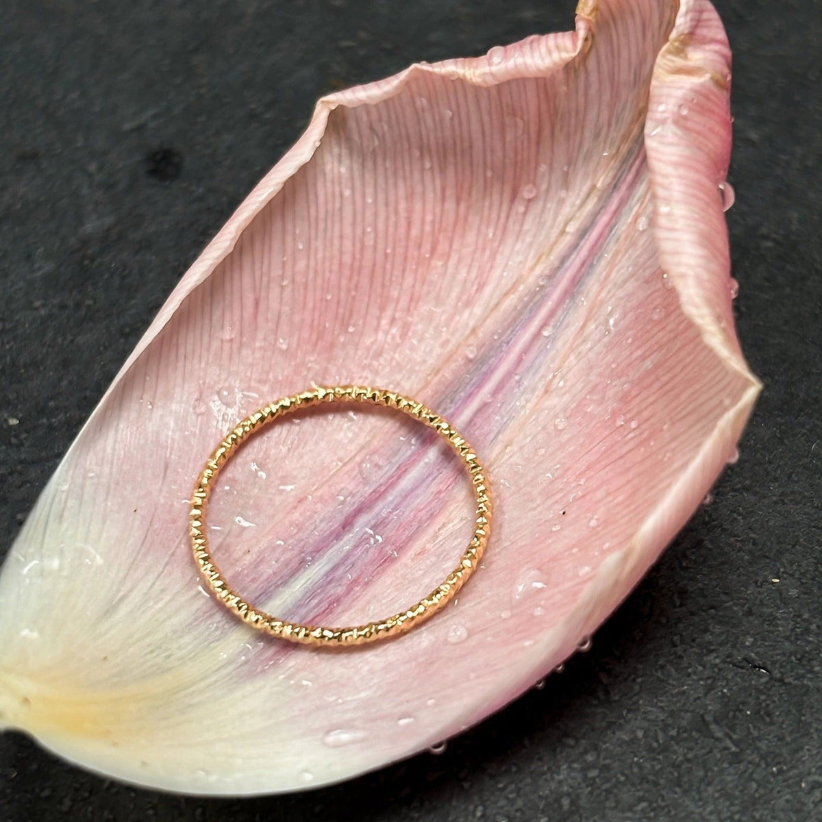 Dainty stacking ring in solid 14k gold resting on a blush tulip petal
