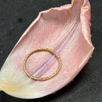 Dainty stacking ring in solid 14k gold resting on a blush tulip petal