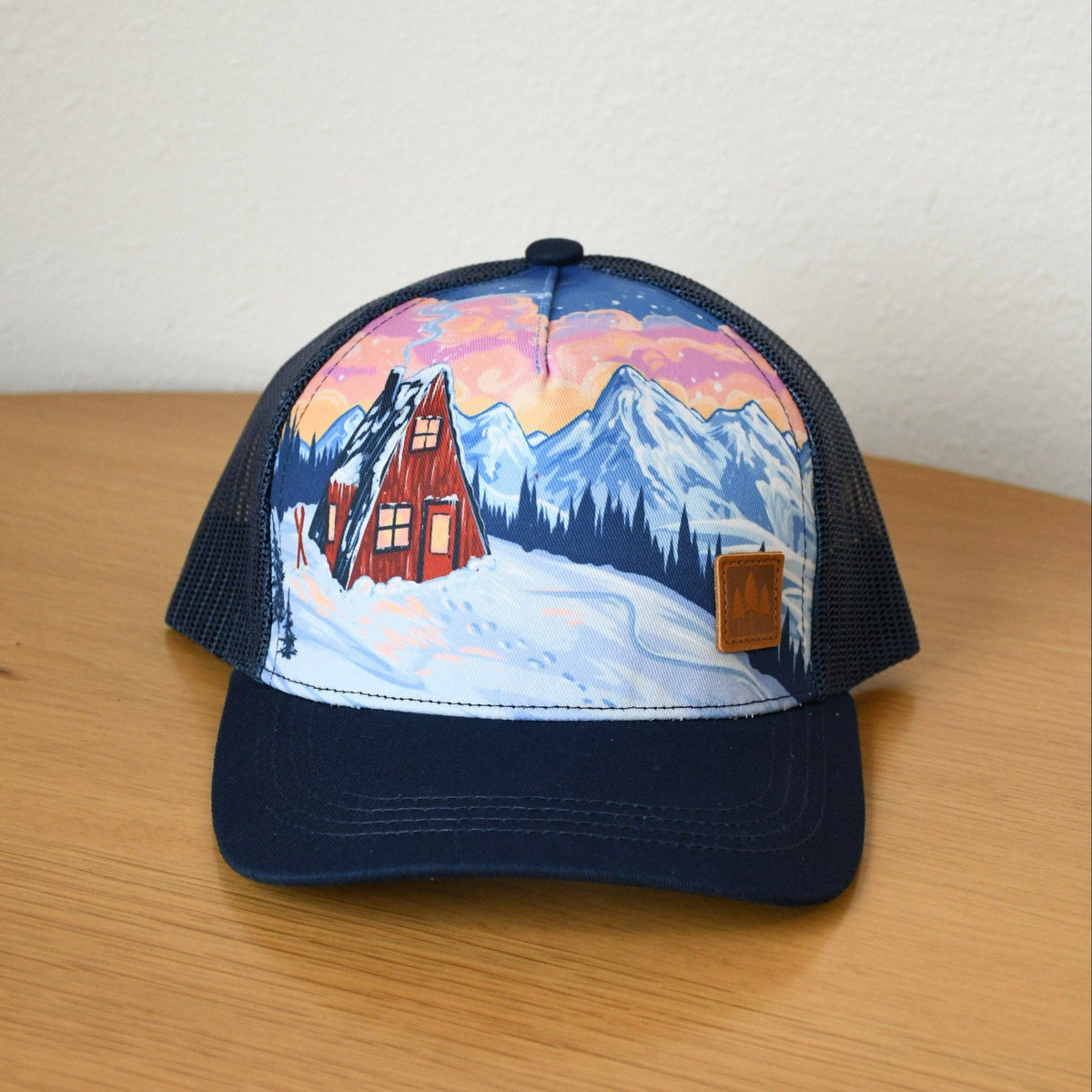 Cap with a mountain and cabin design on a wooden surface