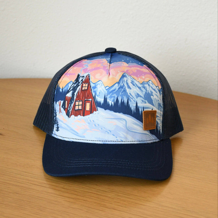 Cap with a mountain and cabin design on a wooden surface