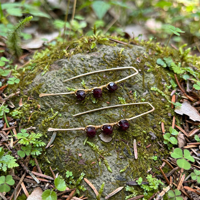Ember Glow Garnet Threader Earrings in 14k gold fill with three faceted garnets wire wrapped on each threader, styled on a mossy forest rock
