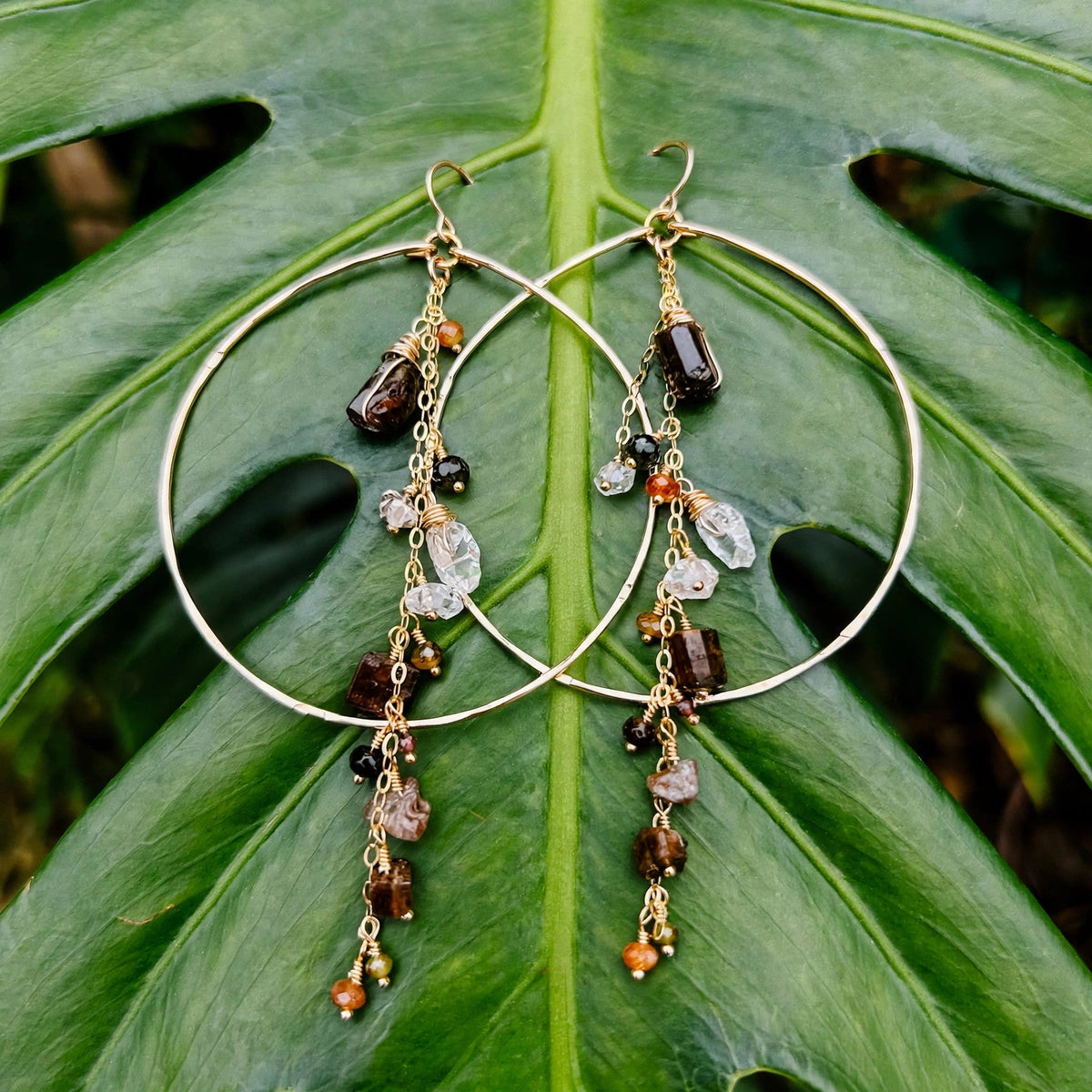 Enchanted Earth Hoop Earrings in 14k gold fill with hammered hoops, resting on a large green leaf
