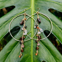 Enchanted Earth Hoop Earrings in 14k gold fill with hammered hoops, resting on a large green leaf
