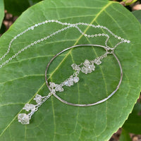 Enchanted Herkimer Diamond Necklace in sterling silver with dangling herkimer diamond quartz crystals, resting on a large green leaf