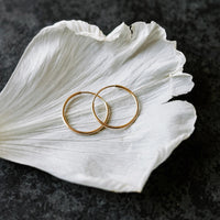 Endless hoop earrings in solid 14k gold, 15mm, resting on a single white petal
