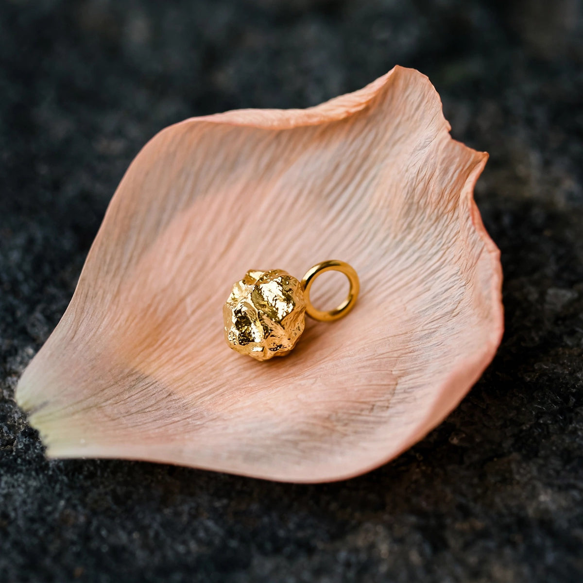Gold nugget charm in solid 14k gold resting on a peach ranunculus petal