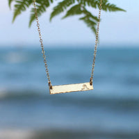Hand Stamped Bar Necklace in 14k gold fill, styled on pale sand at the beach