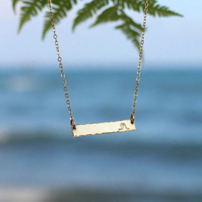 Hand Stamped Bar Necklace in 14k gold fill, styled on pale sand at the beach