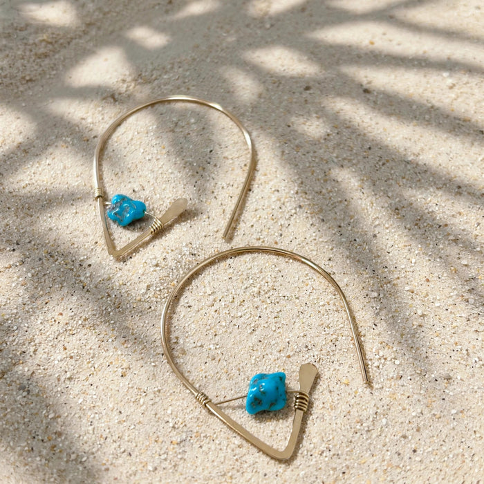 Kingman Turquoise Ear Threaders in 14k gold fill, styled on pale sand at the beach