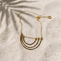Little Rainbow Necklace in 14k gold fill, styled on pale sand at the beach