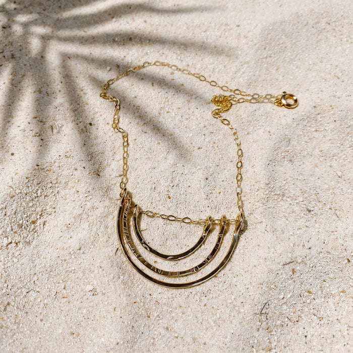 Little Rainbow Necklace in 14k gold fill, styled on pale sand at the beach