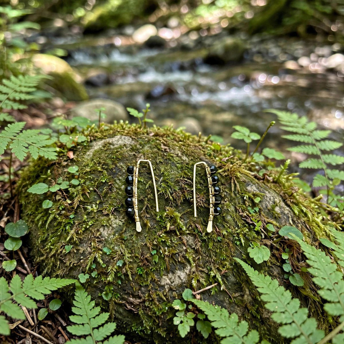 Mini Black Tourmaline Threader Earrings in 14k gold fill with faceted black tourmaline beads wire wrapped along each threader, styled on a mossy rock beside a forest stream