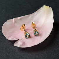 Montana sapphire stud earrings in solid 14k gold resting on a blush peony petal