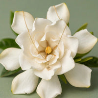 North Star charm necklace in solid 14k gold draped over a white gardenia bloom