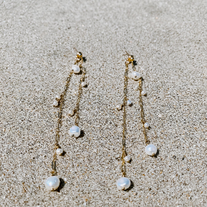 Ocean Eyes Pearl Earrings in 14k gold fill, styled on pale sand at the beach
