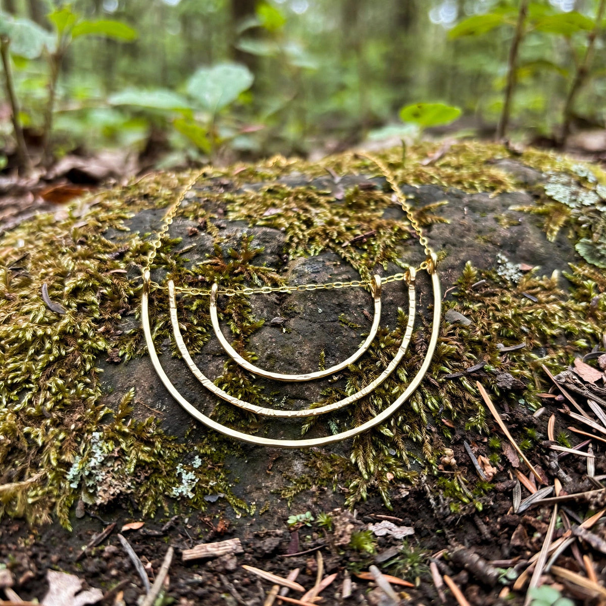 Reflection Rainbow Necklace in 14k gold fill with three hammered rainbow arcs, styled on a mossy rock