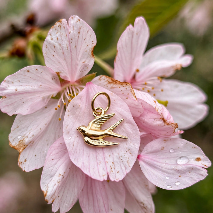 Song bird charm in solid 14k gold resting on a pink cherry blossom