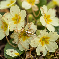 Song bird charm necklace in solid 14k gold, close-up of the bird pendant among primrose blossoms