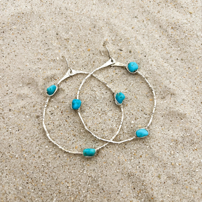 Stargazer Kingman Turquoise Hoop Earrings in sterling silver, styled on pale sand at the beach
