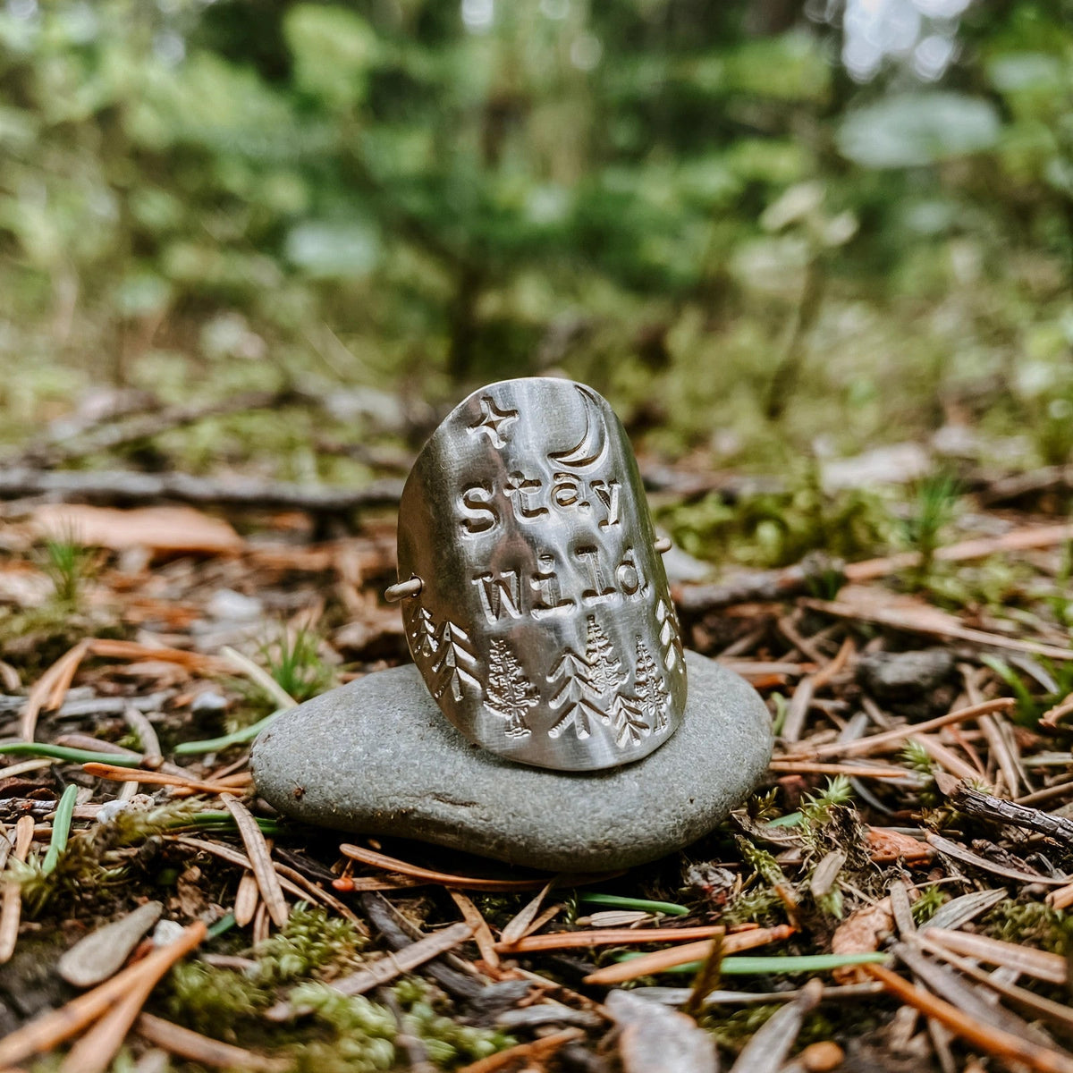 Stay Wild Shield Ring in sterling silver with hand-stamped star, moon and pine trees, styled on a stone