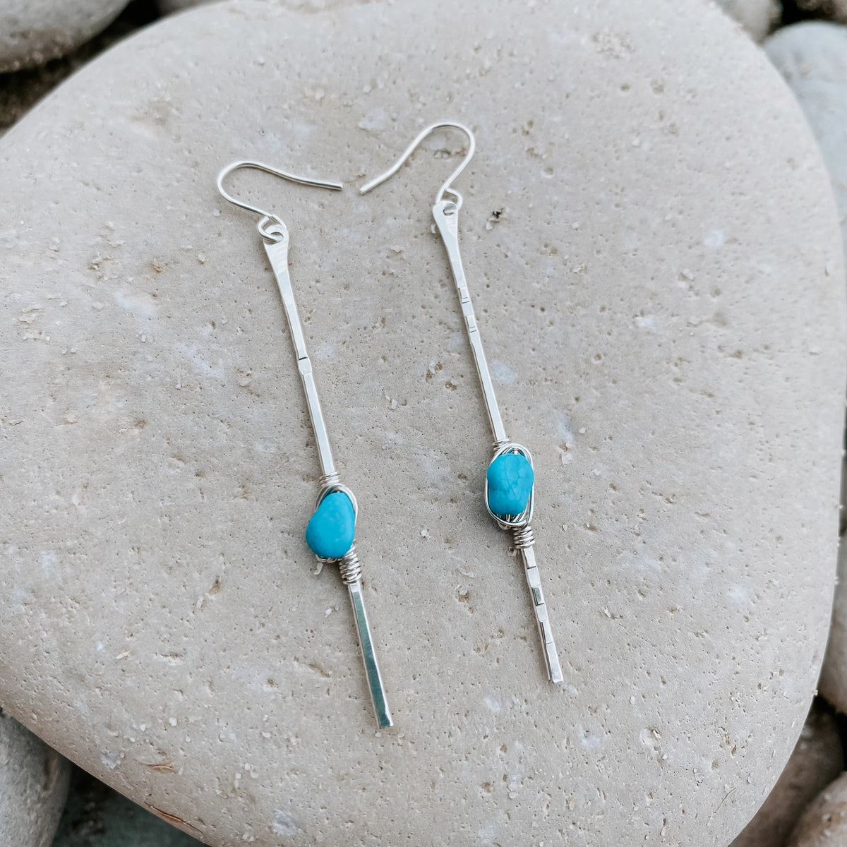 Sticks and Stones Kingman Turquoise Stick Earrings in sterling silver, styled on pale sand at the beach