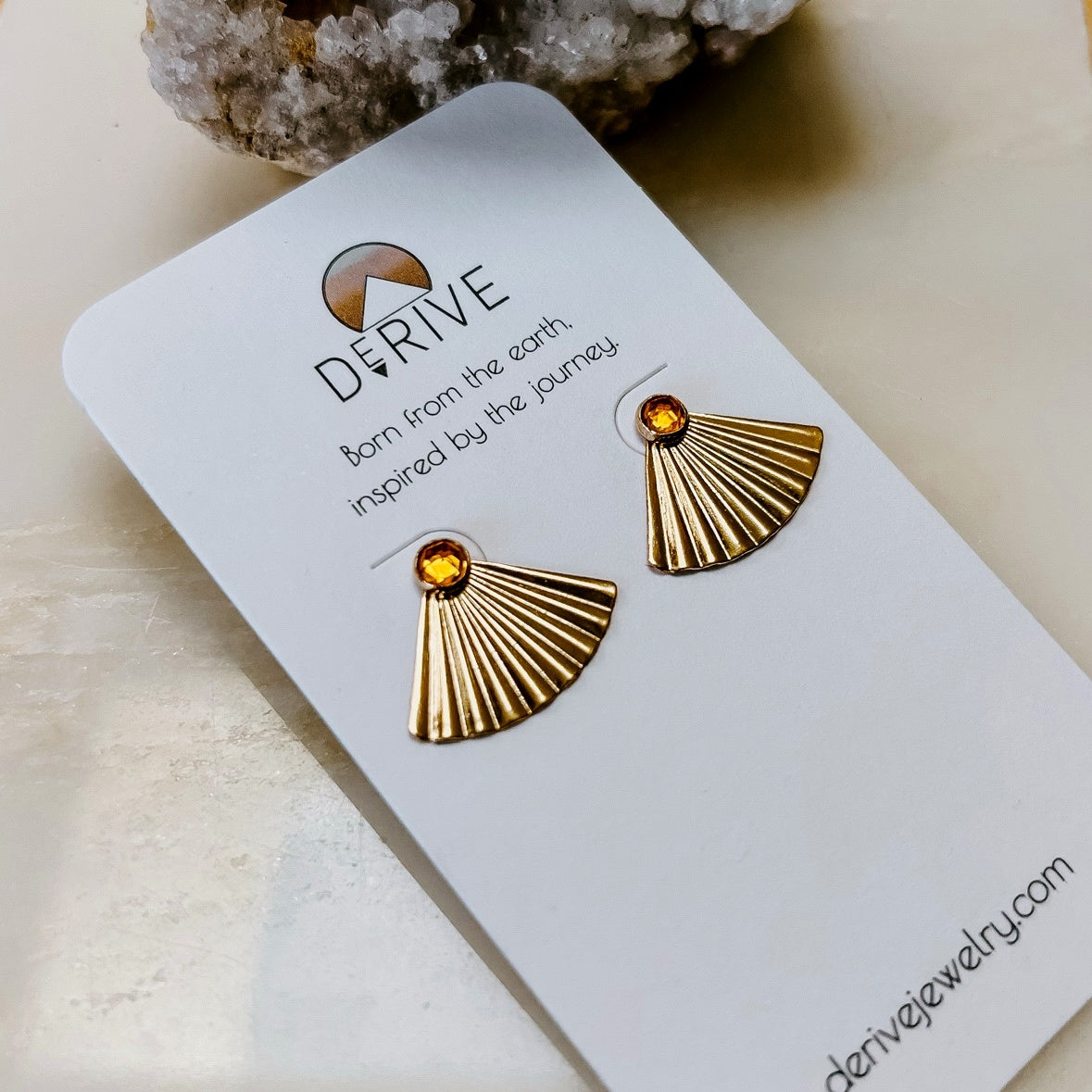 Sunset Citrine Ear Jacket Earrings in 14k gold fill with pleated fan jackets and faceted citrine studs, on a Derive earring card beside a crystal cluster