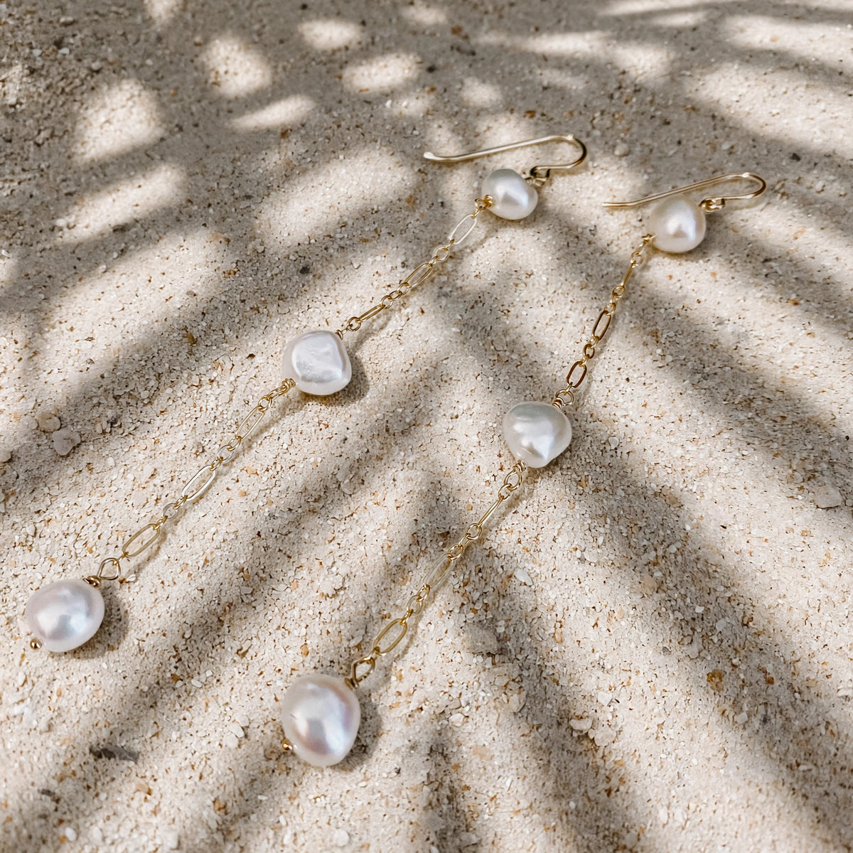 Vahine Pearl Earrings in 14k gold fill, styled on pale sand at the beach
